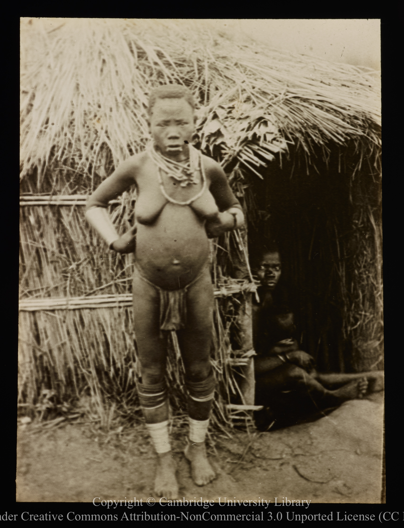 African woman outside thatched building, 1892 - 1914