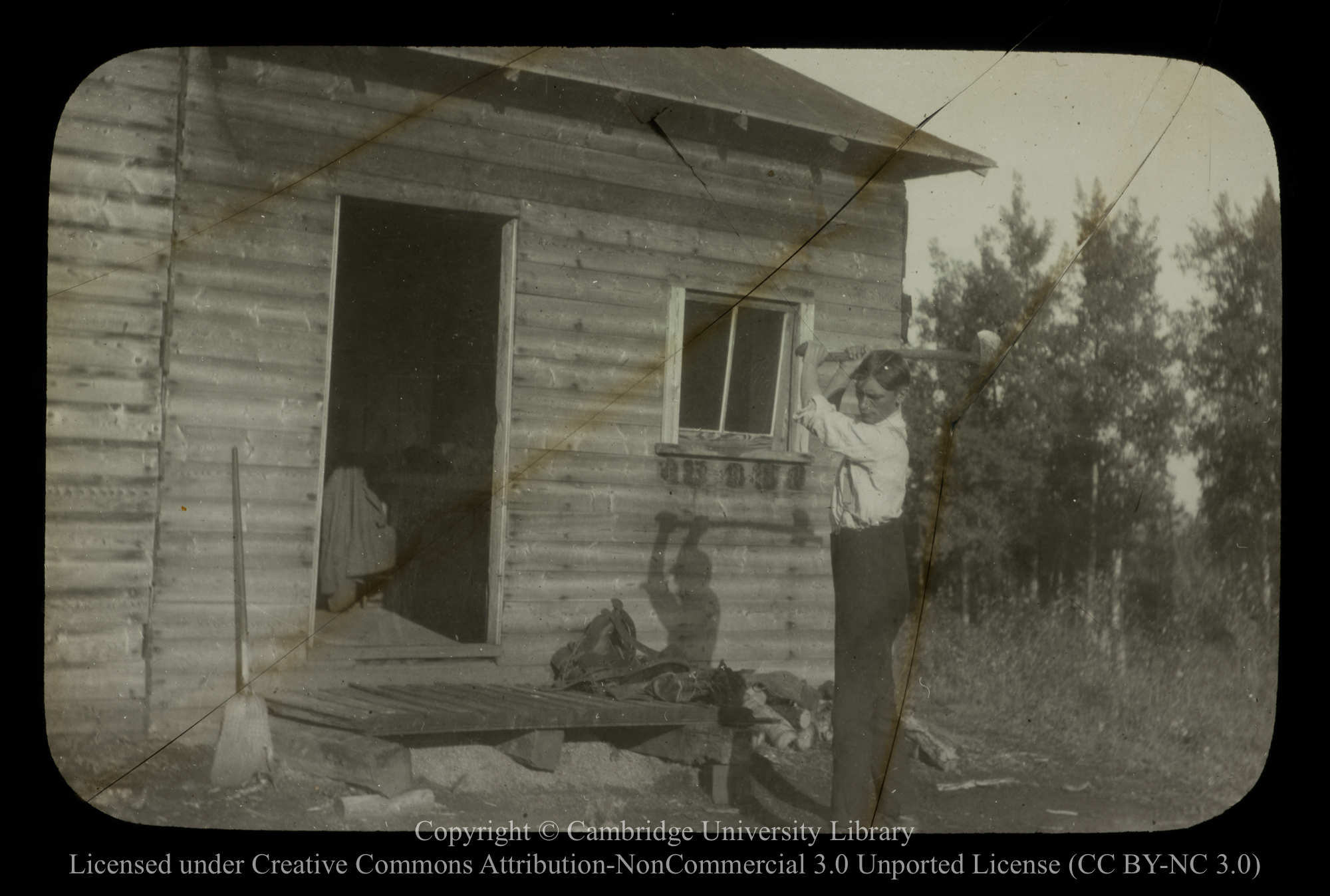 [Man chopping wood outside a cabin], 1910 - 1930